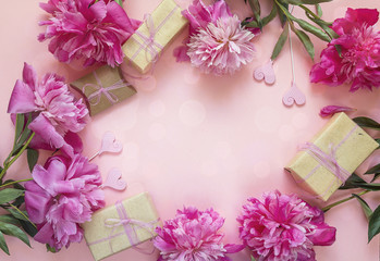 Frame of peonies, gift boxes and decorative hearts on a pink background.