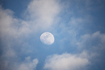 Moon behind slight clouds middle of day