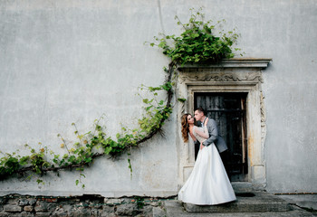 Wedding couple hugs before a wall with greenery