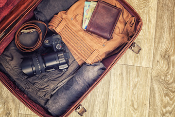 opened suitcase on wooden floor with clothing and vintage camera