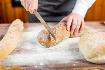 Male hands cutting fresh bread on the wooden table, selective focus