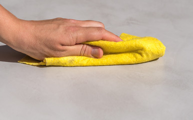woman's hand cleaning spilled water on a cement floor with a yellow floor cloth dishcloth closeup