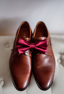 Red bow tie lies on brown leather shoes