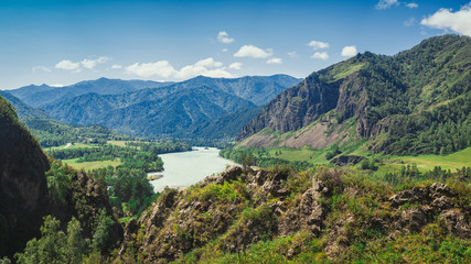 Panorama of the high mountains and the turquoise Katun river in the Altai on a summer clear day. Mountain river between high mountains and coniferous forest, blue sky over mountains