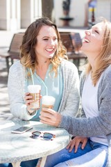 Two friends walk through the city and drink Cappuccino. Two young women sitting in the Cafe. Communication Warm spring. Summer.