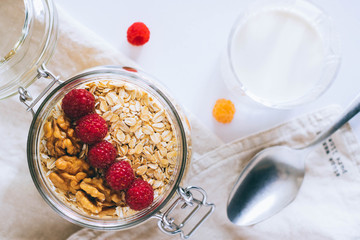 Morning breakfast, oatmeal with red and yellow raspberries and walnuts in a glass jar, a glass of milk, top view