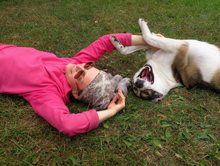 Young woman and a dog are lying on the grass. Everyone is smiling