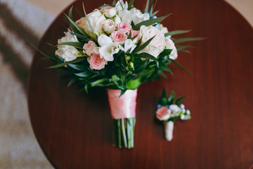 Beautiful bouquet of flowers of the bride and boutonniere lie on the table