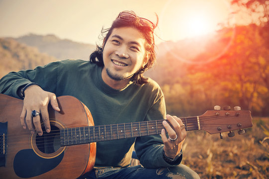 Asian Man Toothy Smiling Face With Happiness Playing Guitar And Sun Set Sky Background