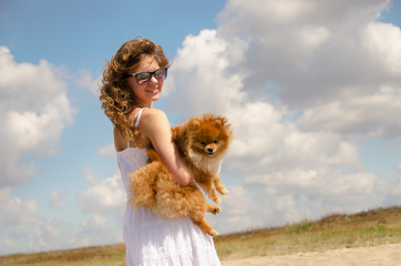 A happy girl with a dog on her hands is standing half a turn. Rest with a pet.