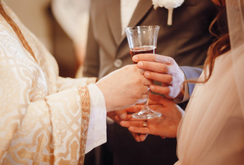 Groom takes glass of wine from priest's arms