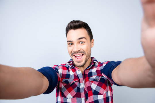 Funky mood of an excited geek young man in casual wear. He is making selfie shot on camera, standing on a pure background, fooling around