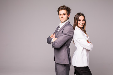 Full length of two young business people standing back to back with hands crossed isolated on grey background