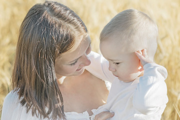 Portrait of a beautiful young mother talking to her small son in wheat field at sunny summer day