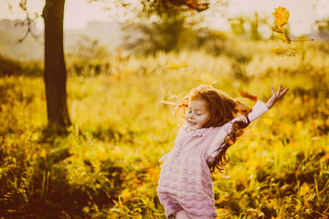 Pretty little girl with red hair plays with fallen leaves