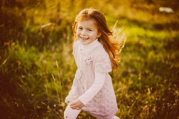 Pretty little girl with red hair plays with fallen leaves