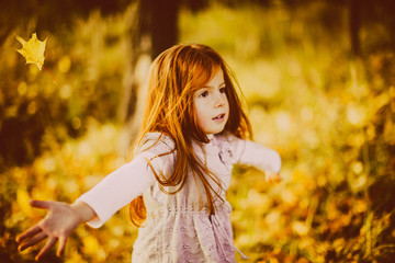 Beautiful little girl with red hair looks happy playing with fallen leaves