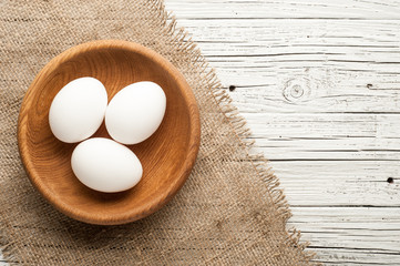 chicken eggs in wooden plate on white wooden background