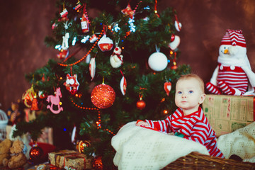 Little boy in stripped pyjamas sits before a Christmas tree