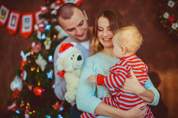 Fototapeta na wymiar Cheerful young parents hold little child posing before a Christmas tree