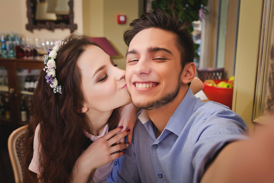 Young enamored couple sitting at a table in a cafe and making selfie