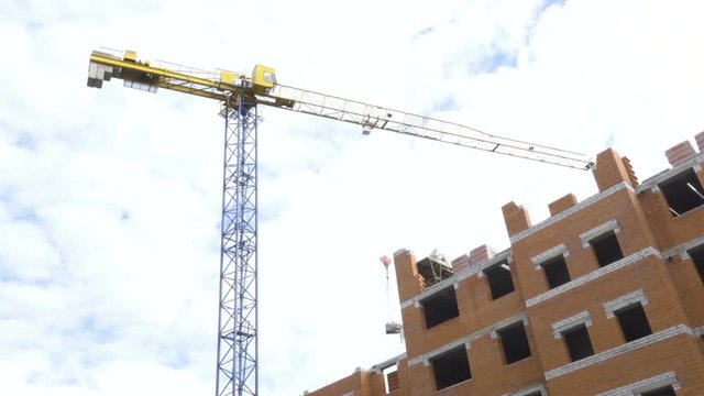 Construction site with workers of high-rise houses of brick tower cranes. Construction site, building of apartments. Construction crane works on construction site, will raise bricks, concrete slabs.