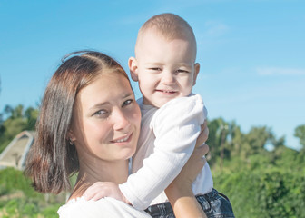 Portrait of a beautiful young mother holding a small baby son in village at sunny summer day