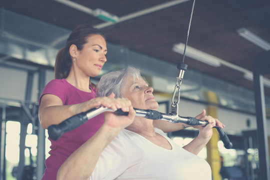 Active senior woman working exercise in the gym. Personal trainer helping senior woman. Workout in gym.