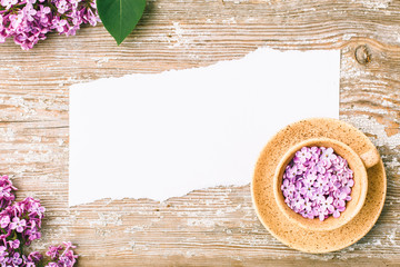 A piece of torn paper and a cup with lilac flowers on an old board