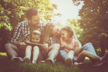 Happy family with two children in meadow using  digital tablet together. Family in meadow.