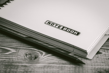 Black and White  .pencil on closed notebook with bookmarks lying on a wooden table