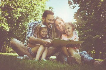 Happy family with two children in meadow reading book together.