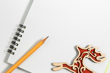 Notebook and yellow pencil with red wooden deer on a white background
