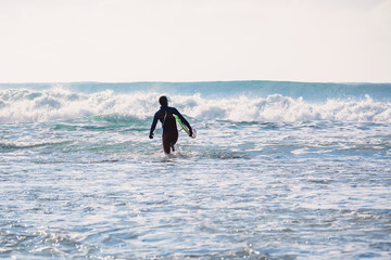 Surfer go to ocean at sunset or sunrise. Surfer in ocean and waves