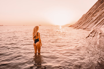 Fototapeta na wymiar Blonde woman in black swimwear relax on quiet sea with warm sunset colors.