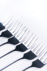 Selective focus closeup macro metal shiny forks lined up over white background