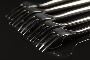 Metal shiny forks isolated over black reflective background with copy space