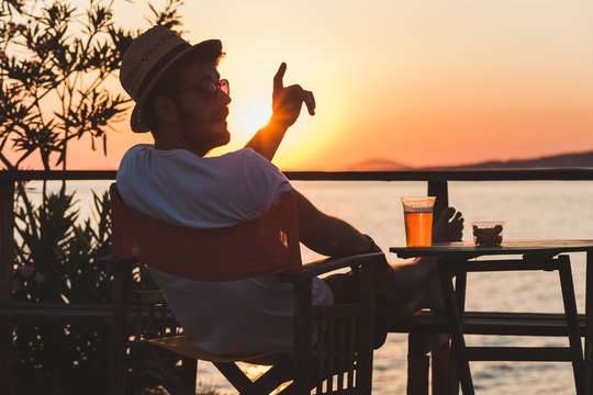 Young man enjoying sunset at a beach bar calling for waiter