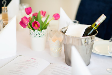 Stół w restauracji z wiaderkiem lodu i winem oraz karta dań menu i dekoracja z tulipanów  - obrazy, fototapety, plakaty