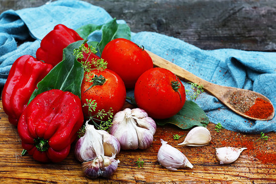 Organic fresh juicy summer vegetables lie on a wooden cutting board: tomatoes, paprika, garlic, herbs and spices in a wooden spoon