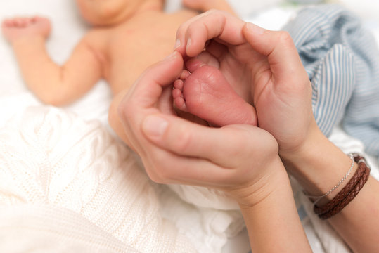 Fragile feet of human baby framed by heart of mothers hands