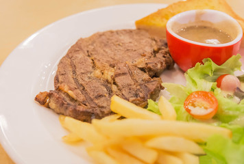 Close up grilled roast pork steak with french fries and vegetables and potatoes on white plate

