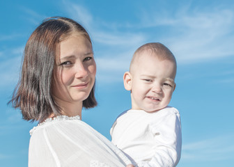 Portrait of a beautiful young mother holding a small baby son. Blue sky background in a summer sunny day