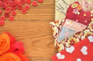 Pieces of fabric with pincushion and red sewing buttons with threads on a wooden board