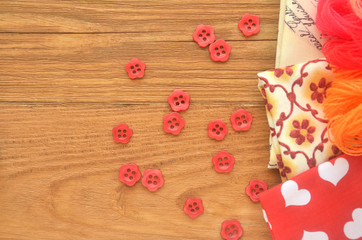 Pieces of fabric with threads and red sewing buttons on a wooden board