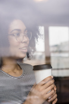 Pensive African American woman drinking coffee behind window