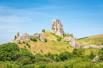 Fototapeta na wymiar Wareham, United Kingdom - June 20, 2017: Ruins of Corfe Castle, built by William the Conqueror in the Isle of Purbeck in Dorset, viewed from the village below. Copy space in blue sky.