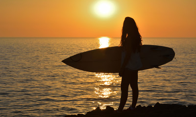 silhouette woman on coast holding surfboard at sunset