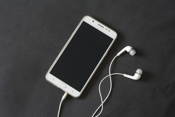 White smartphone with earphones isolated on dark chocolate fabric background. Top view. Perfect for mockup or ads.
