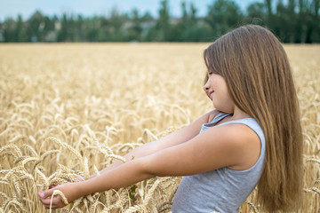 Portrait of adorable little girl with beautiful long hair touching wheat ears in the field on a summer day